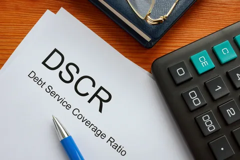 DSCR loan requirements report on a wooden desk beside a blue pen, calculator, and notebook for financial analysis.