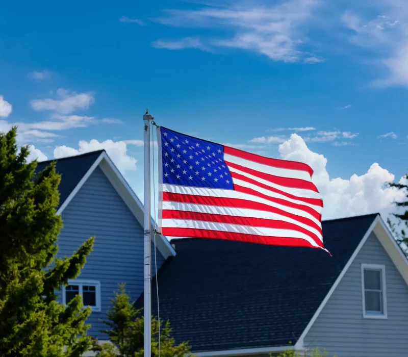 american-flag-waving-next-to-suburban-homes-2026-03-10-00-03-23-utc