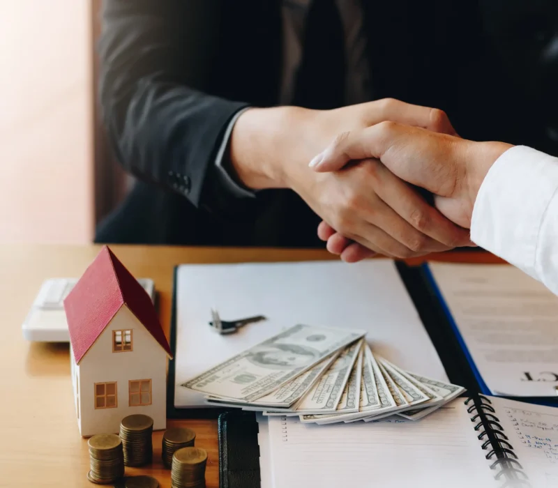 business-handshake-with-house-and-currency-nearby-2026-03-13-01-54-49-utc